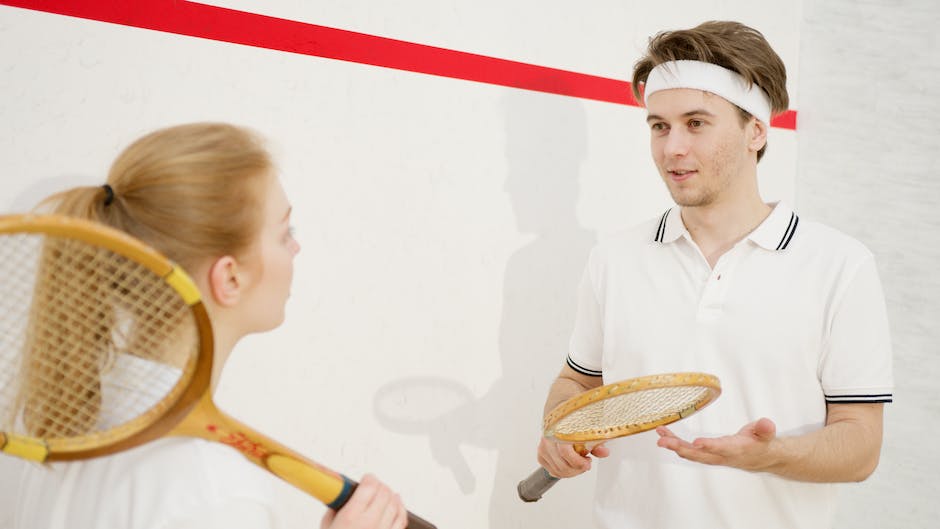 Image of a tennis player holding a tennis racket in a sponsor-branded outfit, standing on a tennis court.